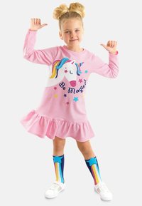 Vaaleanpunainen pitkähihainen mekko, jossa on röyhelöhelma, yksisarvisgrafiikka ja "Ole taianomainen" -teksti. Yhdistetty värikkäiden polvisukkien ja valkoisten kenkien kanssa.