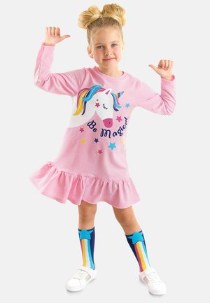 Abito rosa a maniche lunghe con orlo a volant, caratterizzato da una grafica di un unicorno e la scritta "Sii Magico". Abbinato a calze colorate fino al ginocchio e scarpe bianche.