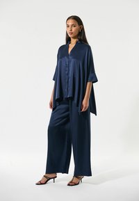 Navy Satin-Outfit mit einer lockeren, kurzärmeligen Bluse mit V-Ausschnitt und weit geschnittenen Hosen. Glatte Textur und elegantes Drapierungsdetail.