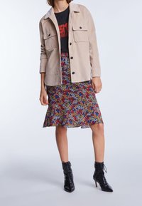 Beige kordväv skjortjacka med framfickor, svart grafisk t-shirt, blommönstrad pennkjol och svarta ankelboots med snörning.
