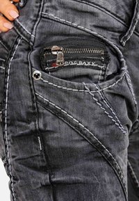 Jeans in denim neri con cuciture bianche, dotati di una piccola tasca con zip sul lato e una texture sbiadita, che migliorano un aspetto robusto.