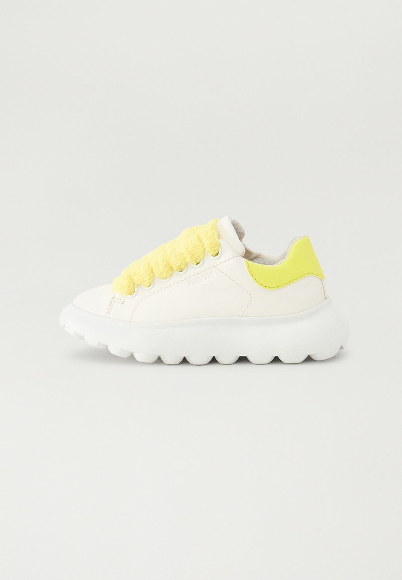 Białe trampki z grubą, teksturowaną podeszwą. Posiadają żółty akcent na pięcie oraz miękkie, żółte sznurowanie w węzeł.