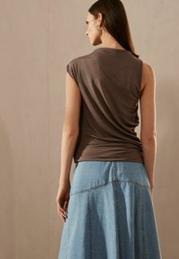 Brun ribbet top med ærmer og et draperet design, parret med en lyseblå denimnederdel med flared snit og synlige syninger.