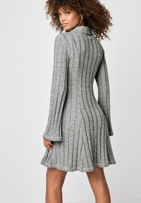 Robe en maille côtelée grise avec de longues manches évasées, un torse ajusté et une jupe évasée. Présente un col et une surface texturée.