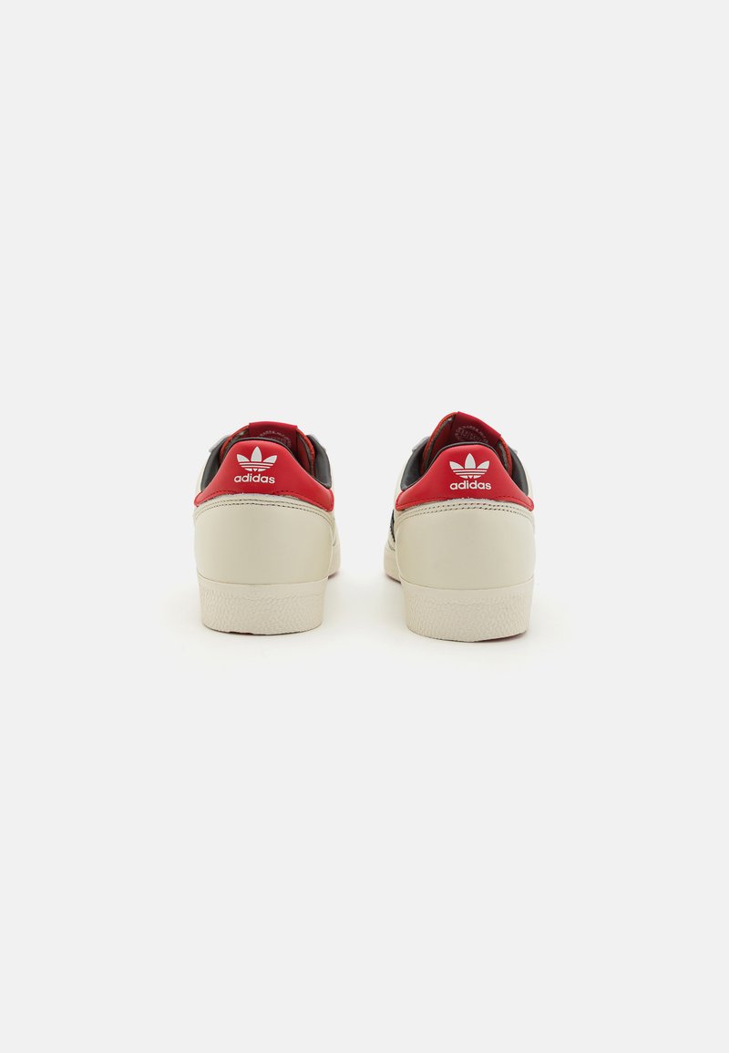 Sneakers in pelle nere, rosse e crema con suole in gomma bianca. Presentano un logo e dettagli sul tallone, progettati per un abbigliamento casual.