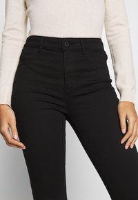 Musta korkeavyötäröiset farkut, joissa on istuva malli, etutaskut ja yksittäinen nappisuljenta vetoketjulla.