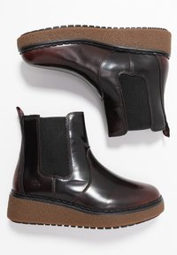 Brązowe lakierowane botki za kostkę z elastycznymi panelami bocznymi i teksturowaną brązową podeszwą platformową. Posiadają logo na zewnętrznej stronie.