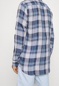 Randig skjorta i blått, vitt och marinblått, med långa ärmar och rundad nederkant. Tillverkad av lättviktsmaterial med knappade manschetter.