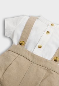 Linnedragt med beige remme og knapper, parret med en hvid kortærmet skjorte med knaplukning og rund halsudskæring.