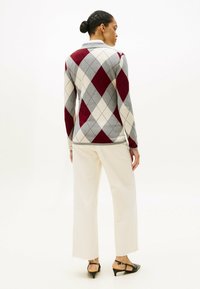 Pullover in maglia argyle rosso e grigio con colletto, abbinato a pantaloni bianchi a gamba larga e décolleté neri con tacco a scomparsa, visto da dietro.