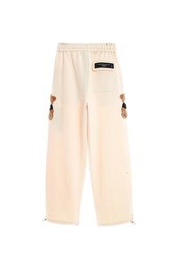 Pantalones de chándal de color melocotón con una cinturilla elástica, bolsillos laterales y adornos en forma de oso en los muslos. La tela es suave y texturizada.