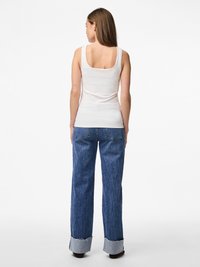 Vit linne med fyrkantig halsringning, kombinerat med högmidjade blå denimjeans med uppvikta benslut och en strukturerad yta.