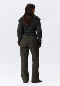 Mørkegrå stripete genser med bred krage, sammen med olivengrønne vide bukser med vertikale striper og to baklommer.