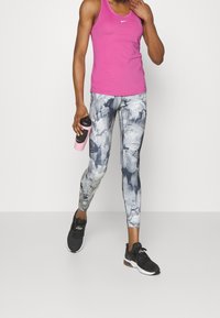 Canotta sportiva senza maniche rosa, leggings attillati a fantasia floreale grigi e bianchi, e scarpe da ginnastica nere con in mano una bottiglia d'acqua rosa.
