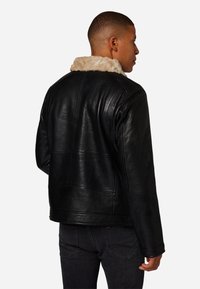 Zwarte leren jas met een nepbontkraag, met een gladde textuur, strakke lijnen en een iets relaxte pasvorm. Achteraanzicht met zichtbare naden.