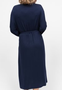 Abito lungo alla caviglia di un blu navy, realizzato in tessuto morbido, con vita cinturata e maniche lunghe, larghe e dal taglio rilassato.