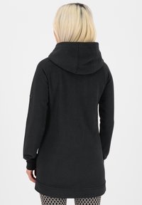 Sudadera negra con capucha de silueta larga, con un bolsillo tipo canguro y puños acanalados. Textura suave, con un diseño minimalista en la manga.