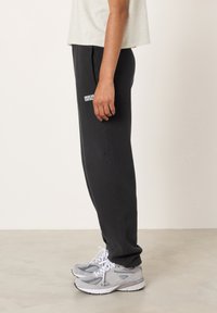 Juodos medvilnės mišinio sportinės kelnės su šoninėmis kišenėmis ir baltu logotipu. Derintos su pilkomis sportbačiais, turinčiais baltus raištelius ir tinklinio akcentus.