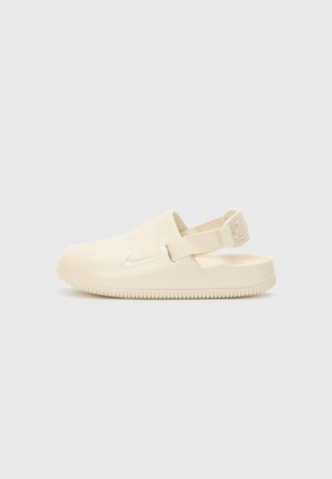 Cremefarvede Nike træskor i mat finish med rygstrop og tekstureret gummisål. Let afrundet tå og minimalistisk design.