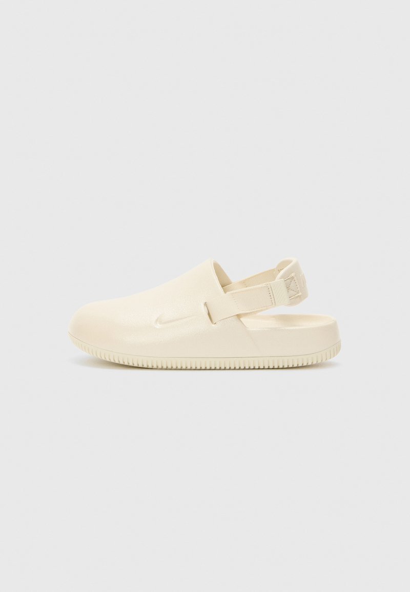 Krém színű, matt felületű Nike klumpák hátsó pánttal és texturált gumitalppal. Enyhén kerek orr és minimalista dizájn.