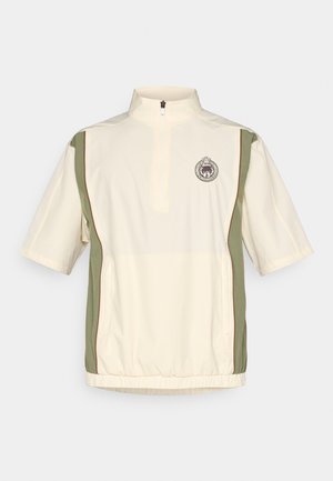 Lahki, krem pulover z zadrgo na vratu, kratkimi rokavi, zelenimi stranskimi paneli, rjavim pasom in značko na prsih.