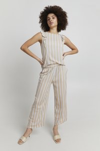 Beige stribet jumpsuit med flæse detaljer på skuldrene, løs pasform, elastisk talje og blød tekstur, parret med lyse slide sandaler.