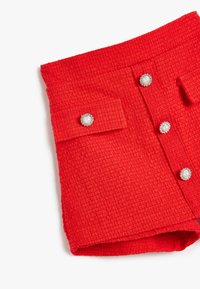 Rode tweed rok met een gestructureerd oppervlak, zes knoopsluitingen en twee klepzakken met parelachtige versieringen.