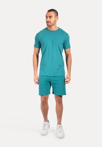 Camiseta atlética color aguamarina y pantalones cortos a juego, fabricados con un material ligero y elástico. Con un diseño de cuello redondo y silueta ajustada. Combinados con zapatillas blancas.