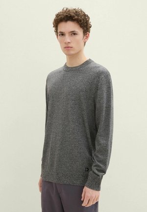 Gray knit sweater with a crew neckline and textured finish. Long sleeves and subtle logo detail near the hem, paired with dark trousers.