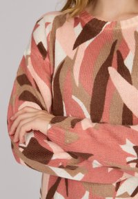 Pull en tricot rose, marron et crème avec un motif de feuilles abstraites. Il présente un col ras du cou et des manches longues avec des poignets côtelés. Texture douce.