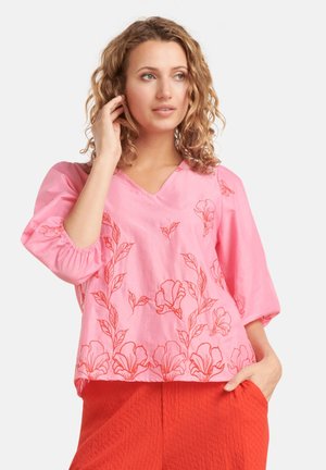 Roze katoenen blouse met V-hals, 3/4 pofmouwen en rode bloemenapplicaties. G gedragen met gestructureerde oranje broek.