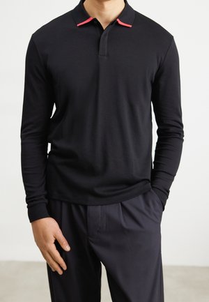 Zwarte lange mouwen polo met een rode accent op de kraag, gemaakt van soepel stof, gecombineerd met donkere, op maat gemaakte pantalons.