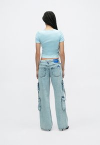 Világoskék testhezálló póló laza világos koptatású farmer cargo nadrággal, oldalzsebekkel és kék márkajelzéssel az derékszalagon.