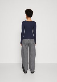 Marinblå långärmad topp med rund hals som är parat med lösa, grå denimbyxor med kontrasterande svarta sidopaneler och synlig sömnad.