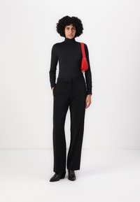 Melnā turtlenecka augšdaļa kopā ar veidotiem melniem biksēm, kam ir sānu kabatas, un akcents ar mazu sarkanu rokassomu un melnām augstpapēžu zābakiem.