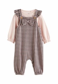 Camicia a maniche lunghe rosa sotto una salopette a quadri con dettaglio a fiocco, dotata di spalline arricciate, bottoni e polsini arricciati. Il materiale sembra morbido.