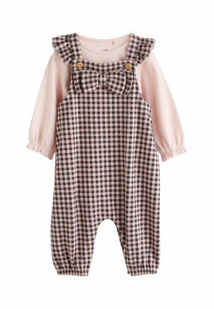 Rosa Langarmshirt unter einem karrierten Overall mit einer Schleifendetail, mit Rüschenträgern, Knöpfen und gerafften Manschetten. Das Material wirkt weich.