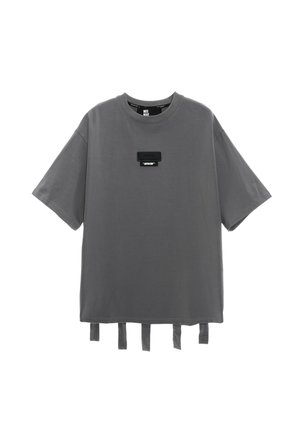 Camiseta gris de manga corta, con un escote redondo, un parche rectangular negro en el pecho y detalles de cinta en el dobladillo inferior.