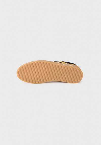 Black sneaker sole with a textured gum rubber surface, featuring horizontal grooves for grip and support. Leather and fabric upper.