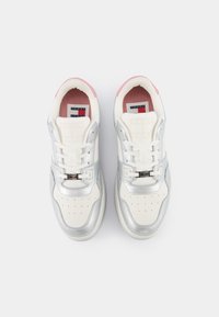 Baskets blanches avec des accents argentés et un talon rose. Le design comprend des perforations sur l'avant et une fermeture à lacets avec un détail de logo.