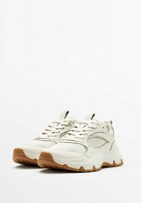 Sneaker di colore chiaro con un design testurizzato, suola in gomma e accenti bruniti a contrasto. Presentano lacci e linguetta imbottita per il comfort.