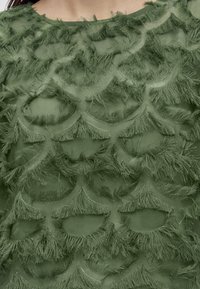 Gros plan sur un tissu vert avec un motif texturé festonné doté de bords doux et effilochés sur un vêtement.