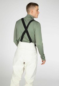 Olijfgroene top met lange mouwen en zwarte bretels, gecombineerd met hoogzaak witte broek, die een gladde textuur laat zien.