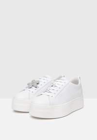 Baskets plateformes en cuir blanc ornées d'un embellissement en forme de fleur, de deux accents en perle, avec une finition lisse et brillante.