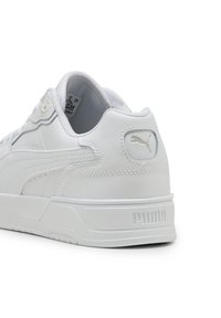 Sneaker bianco in pelle con finitura testurizzata, dotata di colletto imbottito, dettagli perforati e un branding sottile sul tallone e sul lato.
