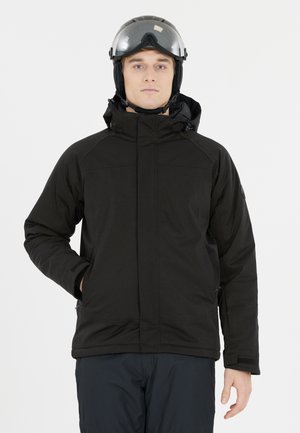 Schwarze isolierte Jacke mit hohem Kragen, Reißverschlusstaschen und lockerer Passform. Das Modell trägt einen silbernen Skihelm. Schlichtes Design, keine Muster.