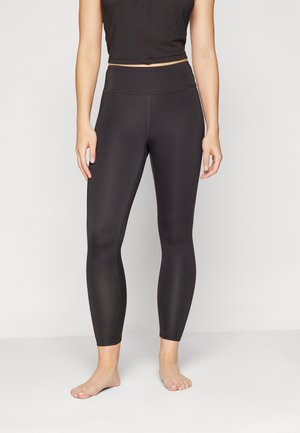 Leggings noirs avec une taille haute, fabriqués en tissu extensible et lisse. Présentent un design ajusté, des côtés sans couture et aucune visiblité de matériel.