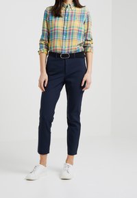 Camicia a quadri gialla, blu e verde, abbinata a pantaloni slim-fit blu navy e sneakers bianche; include una cintura nera e dettagli con bottoni.