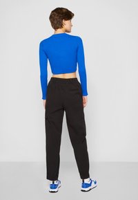 Blue ribbed cropped long-sleeve top paired with black cargo pants featuring side pockets and elastic cuffs, worn with white and blue sneakers.