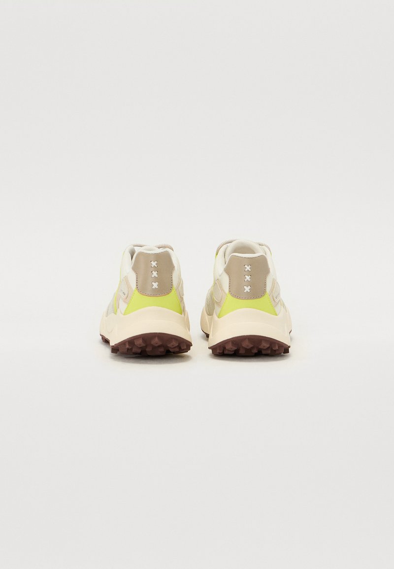 Des chaussures de sport multicolores avec une tige beige et jaune. Elles présentent un matériau texturé, un col rembourré et une semelle extérieure robuste et marron.